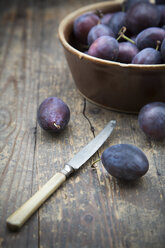 Earthenware bowl with plums and a knife on wooden table, studio shot - LVF000231