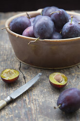 Earthenware bowl with plums and a knife on wooden table, studio shot - LVF000232