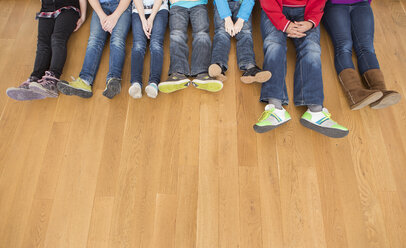 Austria, children and teenager sitting on a wooden floor showing their legs - DISF000093