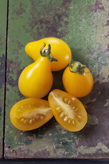 Geschnittene und ganze gelbe Birnentomaten (Solanum lycopersicum) auf grünem Holz, Studioaufnahme - CSF020165
