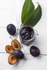 Glass of plum jam and some plums on plastic spoon, studio shot - CSF020157