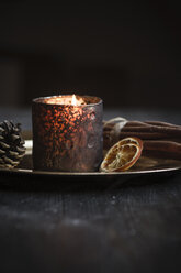 Weihnachtsdekoration mit Teelicht, Zimtstangen, Scheiben von getrockneten Orangen und Zapfen auf Teller, Studioaufnahme - SBD000267