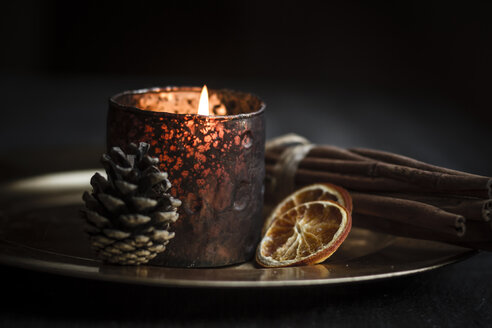 Weihnachtsdekoration mit Teelicht, Zimtstangen, Scheiben von getrockneten Orangen und Zapfen auf Teller, Studioaufnahme - SBD000266
