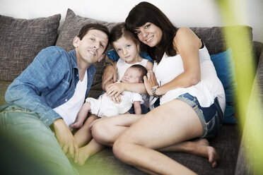 Junge Familie mit männlichem Neugeborenen und kleiner Tochter, die zu Hause auf dem Sofa sitzt - JATF000381