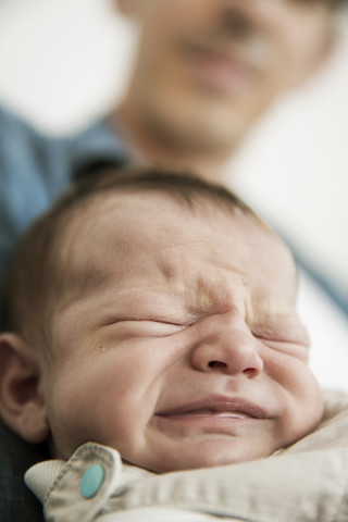Junger Vater hält seinen weinenden neugeborenen Sohn, lizenzfreies Stockfoto
