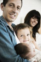 Junge Familie mit männlichem Neugeborenen und kleiner Tochter, die zu Hause auf dem Sofa sitzt - JATF000385