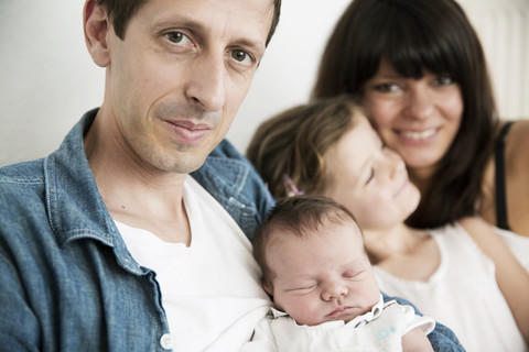 Junge Eltern mit männlichem Neugeborenen und kleiner Tochter sitzen zu Hause auf dem Sofa, lizenzfreies Stockfoto