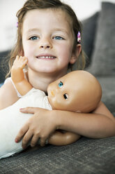 Portrait of smiling little girl lying on sofa with her doll, close-up - JATF000390