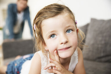 Porträt eines kleinen Mädchens auf dem Sofa liegend, ihr Vater steht im Hintergrund - JATF000392