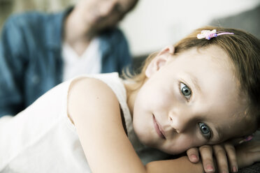 Nachdenkliches kleines Mädchen auf dem Sofa liegend, ihr Vater steht im Hintergrund - JATF000394