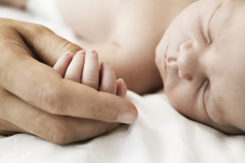 Mutter hält die Hand ihres schlafenden neugeborenen Sohnes, lizenzfreies Stockfoto