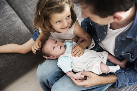 Junger Vater mit männlichem Neugeborenen und kleiner Tochter sitzt zu Hause auf dem Sofa, lizenzfreies Stockfoto