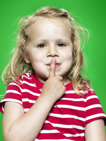 Portrait of little girl with forefinger on her lips, studio shot stock photo