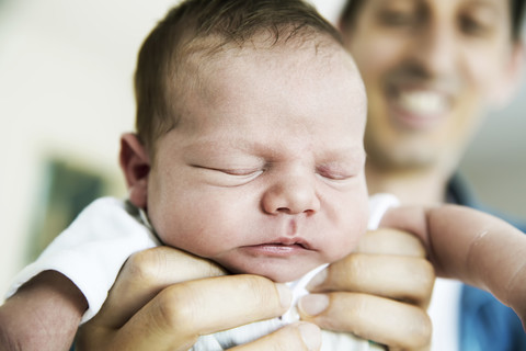 Lächelnder junger Vater hält seinen schlafenden neugeborenen Sohn, lizenzfreies Stockfoto