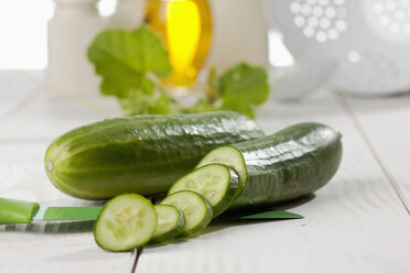 Small sliced and whole cucumbers with knife on white wooden table, studio shot - CSF020176