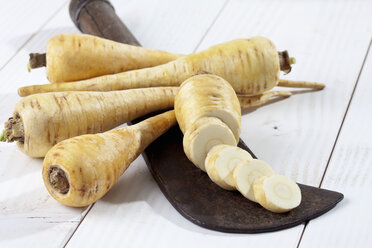 Sliced and whole parsnips (Pastinaca sativa) with antique knife on white wooden table, studio shot - CSF020183