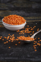 Red lentils in small white bowl and a spoon on dark surface, close-up - SBDF000271