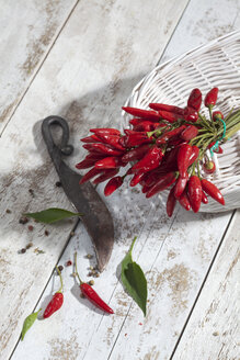Rote Chilischoten (Capsicum) in weißem Korb auf weißem Holztisch, Studioaufnahme - CSF020239