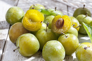 Geschnittener und ganzer Grünkern (Prunus domestica subsp. italica var. claudiana) auf weißem Holztisch, Studioaufnahme - CSF020243