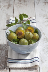 Sliced and whole greengages (Prunus domestica subsp. italica var. claudiana) in a bowl on white wooden table, studio shot - CSF020244