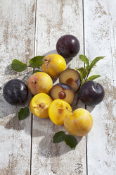 Sliced and whole yellow and black gages (Prunus domestica subsp. italica) on white wooden table, studio shot - CSF020251