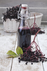 Holunderbeeren (Sambucus), Korb und eine Flasche Holundersaft auf weißem Holztisch, Studioaufnahme - CSF020284