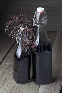 Holunderbeeren (Sambucus) und zwei Flaschen Holundersaft auf Holztisch, Studioaufnahme - CSF020264