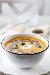 Pumpkin soup in old bowl garnished with pumpkin seed oil, pumpkin seeds and sour cream, studio shot - CSF020266