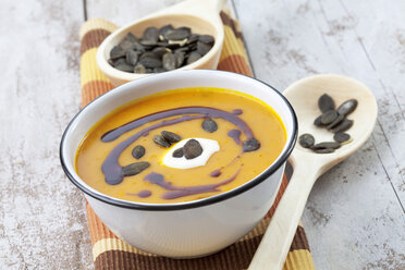 Pumpkin soup in old bowl garnished with pumpkin seed oil, pumpkin seeds and sour cream, studio shot - CSF020271