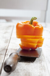 In Scheiben geschnittene orangefarbene Paprika (Capsicum), gestapelt auf einem Schneidemesser, Studioaufnahme - CSF020297