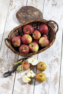 Bio-Äpfel (Malus), Korb, Holzlöffel und ein Messer auf weißem Holztisch, Studioaufnahme - CSF020301