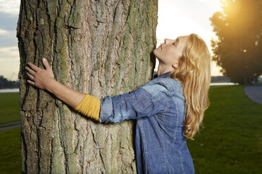 Germany, Dusseldorf, Young woman hugging tree - STKF000473