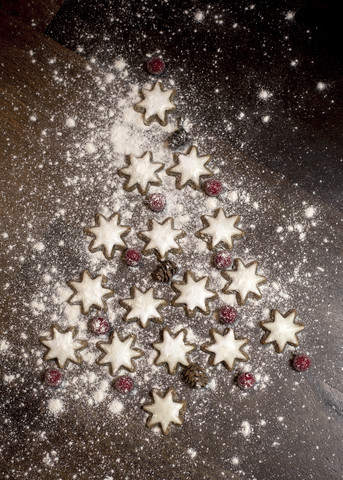 Christmas tree formed of star-shaped cinnamon cookies, red berries and fir cones on wooden table stock photo