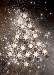 Christmas tree formed of star-shaped cinnamon cookies, red berries and fir cones on wooden table - SARF000133