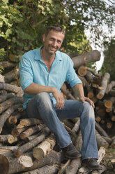 Deutschland, Bayern, Lächelnder Mann sitzt auf Holzstapel - CRF002497