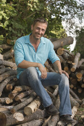 Germany, Bavaria, Smiling man sitting on woodpile - CRF002497