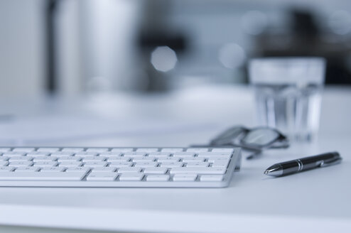 Tastatur auf dem Schreibtisch, Wasserglas, Kugelschreiber und Brille - ASF005211