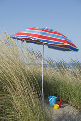 Italien, Adria, Schaufel und Eimer im Sonnenschatten auf einer Sanddüne mit Gras - CRF002503