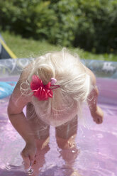 Girl playing with spoon in paddling pool - TCF003644