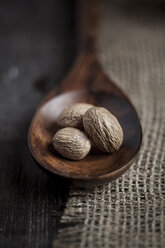 Three nutmegs on wooden spoon on burlap, studio shot - SBDF000304