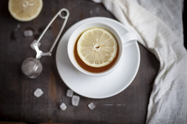 Tasse Tee mit Zitronenscheibe, Kandiszucker und Teesieb auf Holztisch, Studioaufnahme - SBDF000312