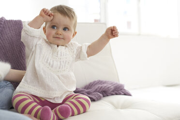 Lächelndes kleines Mädchen mit ausgestreckten Armen auf dem Sofa sitzend - FSF000023