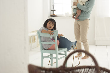 Kleines asiatisches Mädchen sitzt auf einem Stuhl, Mutter und Schwester im Hintergrund - FSF000091