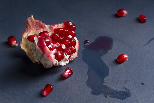 Kerne und Stück Granatapfel [Punica granatum] auf blauem Holz, Nahaufnahme - MYF000059