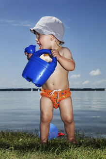 Baby boy with watering can in front of lake - RDF001199