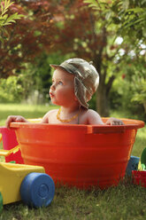 Kleiner Junge badet in orangefarbener Wanne im Garten - RDF001202