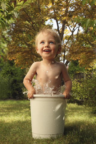 Kleiner Junge badet im Eimer im Garten, lizenzfreies Stockfoto