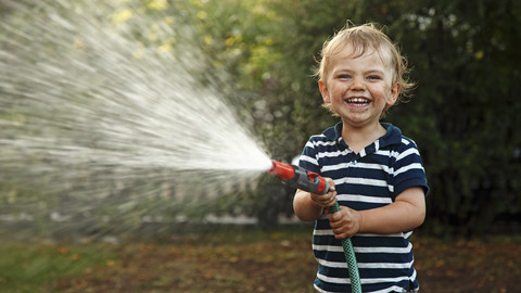 Portrait of little boy splashing with garden hose stock photo