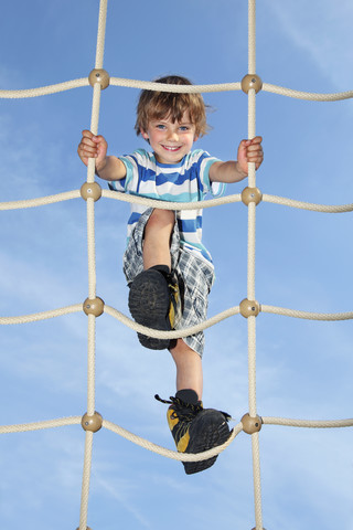 Porträt eines lächelnden kleinen Jungen, der auf einem Kletternetz steht, lizenzfreies Stockfoto