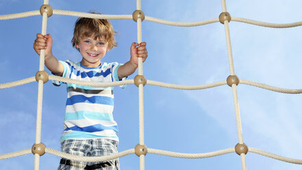 Portrait of smiling little boy standing on climbing net - RDF001224